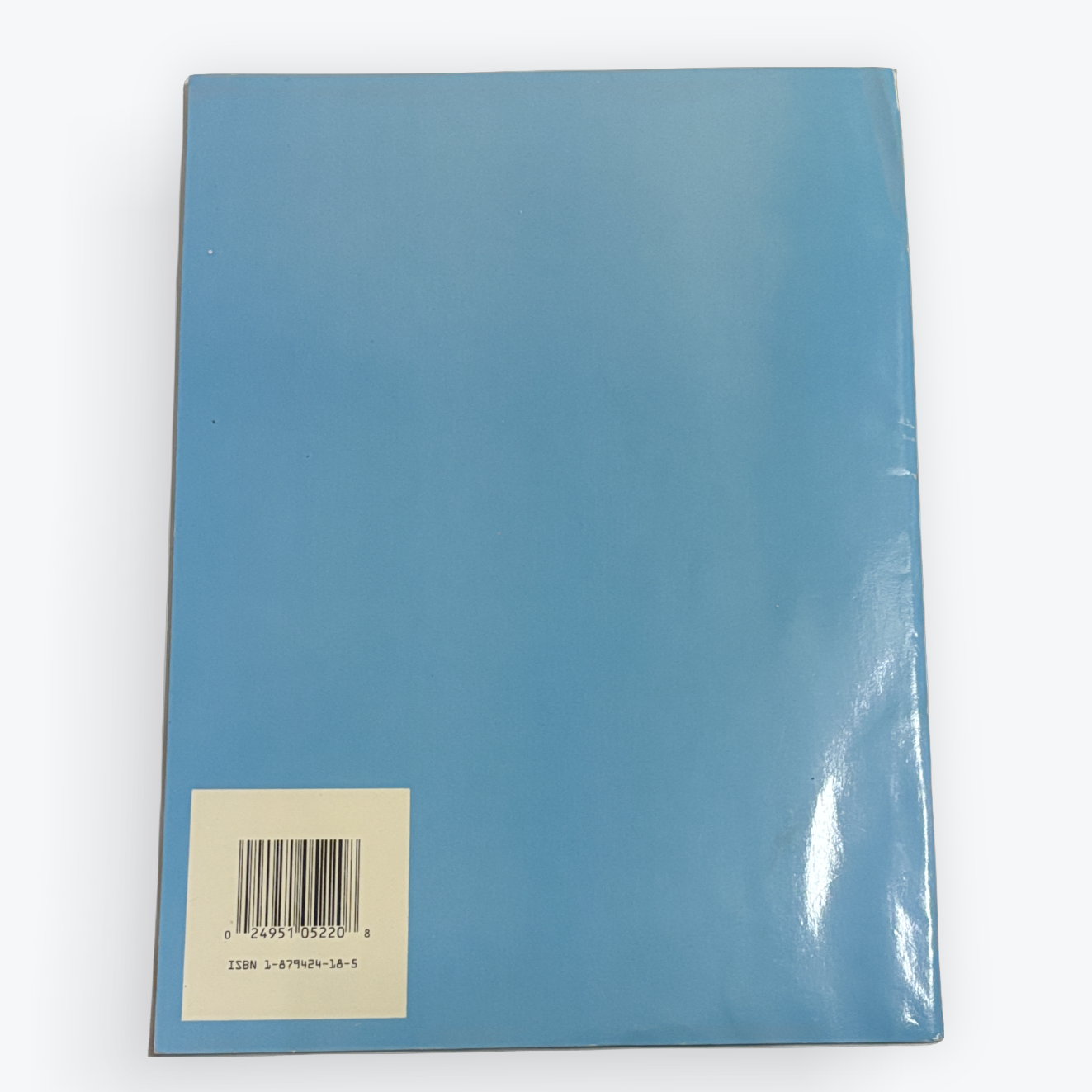 The back cover of a glossy blue notebook or book, featuring a white square label with a barcode near the bottom left, set against a plain white background.
