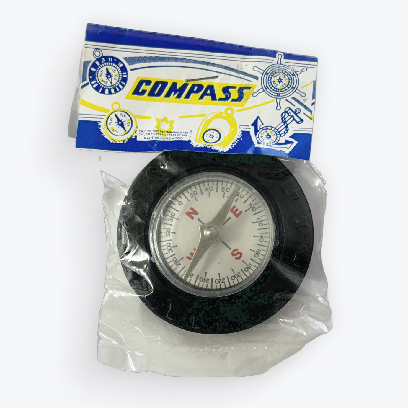 A small round compass inside a clear plastic bag with a blue, white, and yellow cardboard header card. The compass has a black outer ring, a white dial face, and silver and red needle elements.
