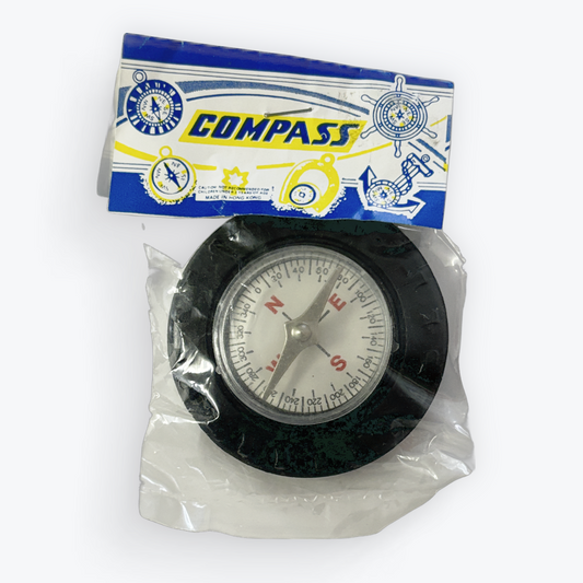 A small round compass inside a clear plastic bag with a blue, white, and yellow cardboard header card. The compass has a black outer ring, a white dial face, and silver and red needle elements.